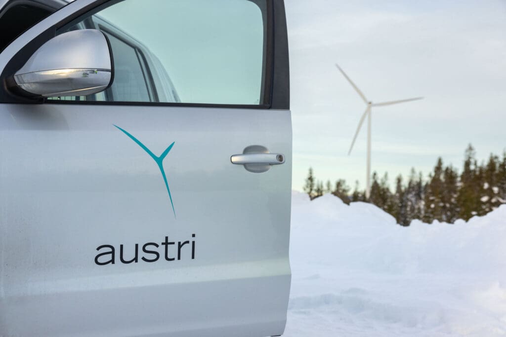Bildet viser logoen til Austri Vind på en bil foran en vindmølle